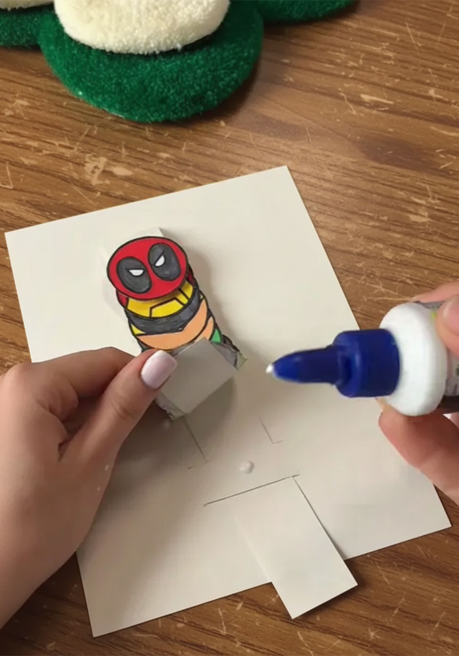 Threading the superhero accordion strip through the card slits during DIY pop-up Father's Day card assembly	phase 3 step 4
