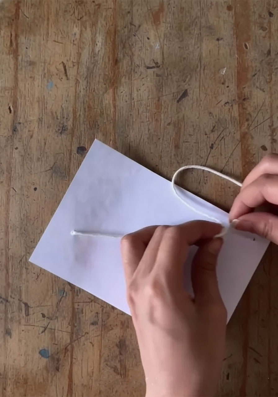 Adult hands threading white twine through two holes in cardstock to create the pull-string mechanism for a DIY Father's Day card step4b