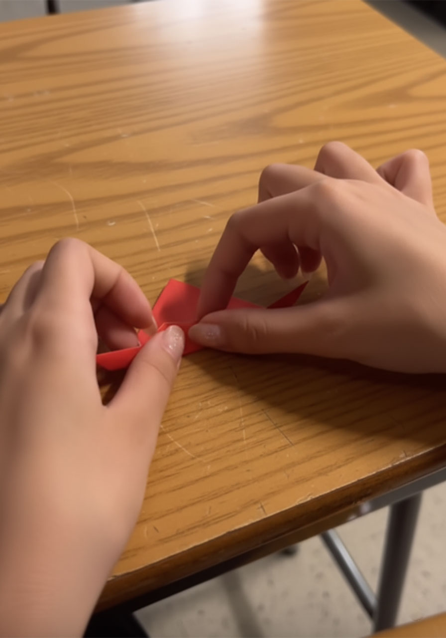Hands gluing small wooden buttons and a red paper pocket square onto a blue paper suit jacket Father's Day card on a white table step4e