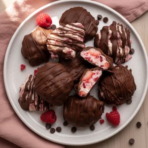 Plate of chocolate covered strawberry Greek yogurt clusters with creamy frozen yogurt filling visible, garnished with fresh raspberries