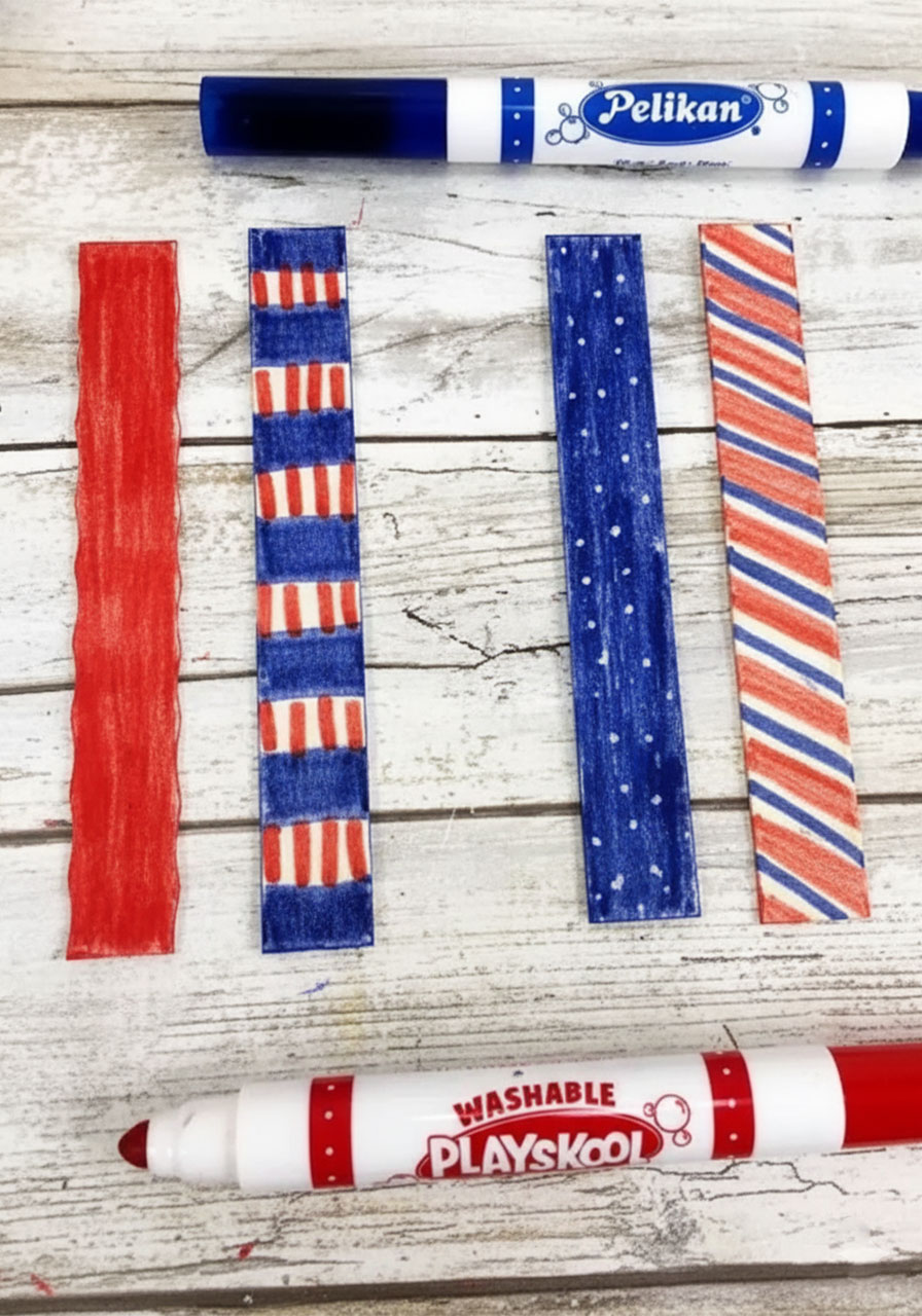 Four jumbo craft sticks trimmed flat and colored in red and blue marker patterns for the popsicle stick fireworks handle — Step 3 of the coffee filter watercolor fireworks craft