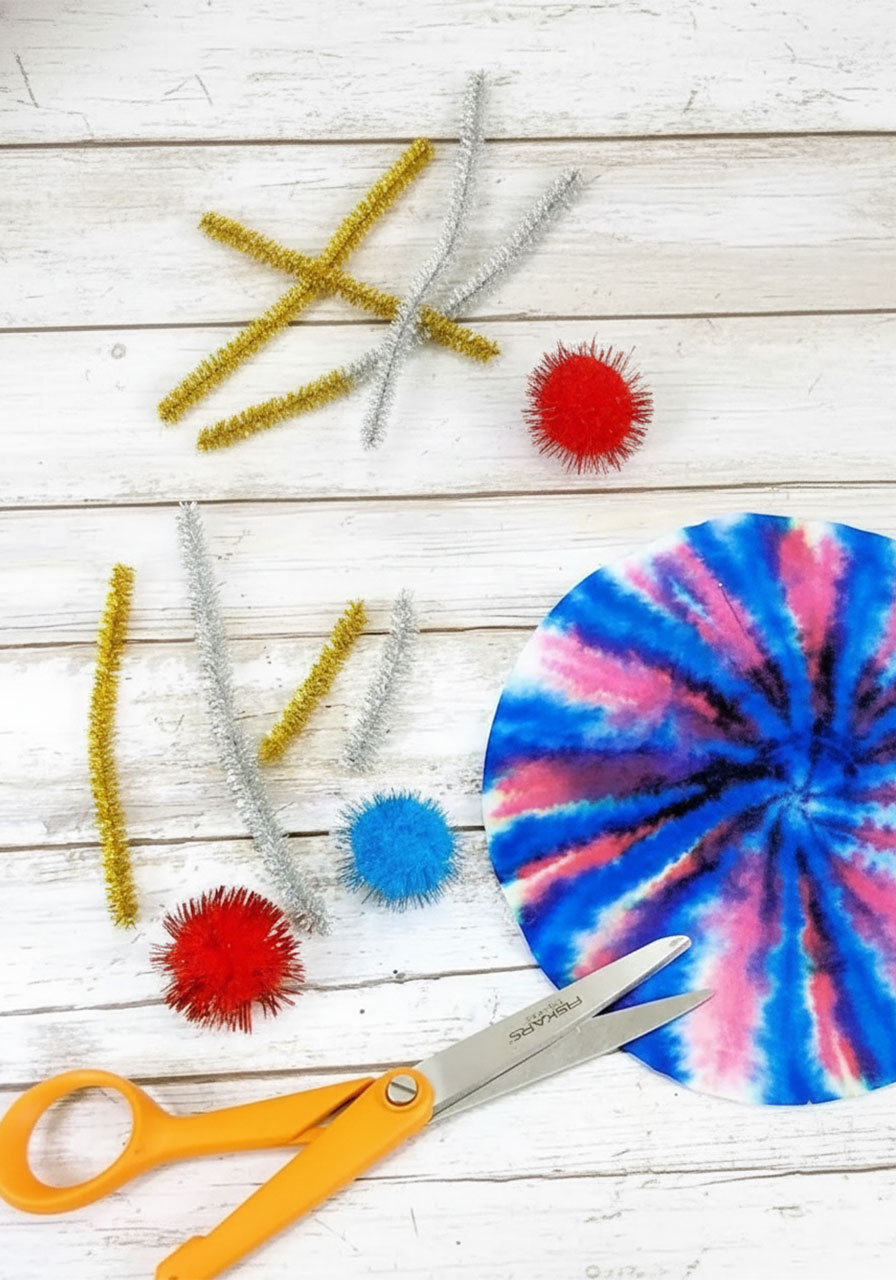 Cut gold and silver pipe cleaner pieces and red and blue sparkle pom poms laid out ready for assembly — Step 4 of the coffee filter watercolor fireworks craft