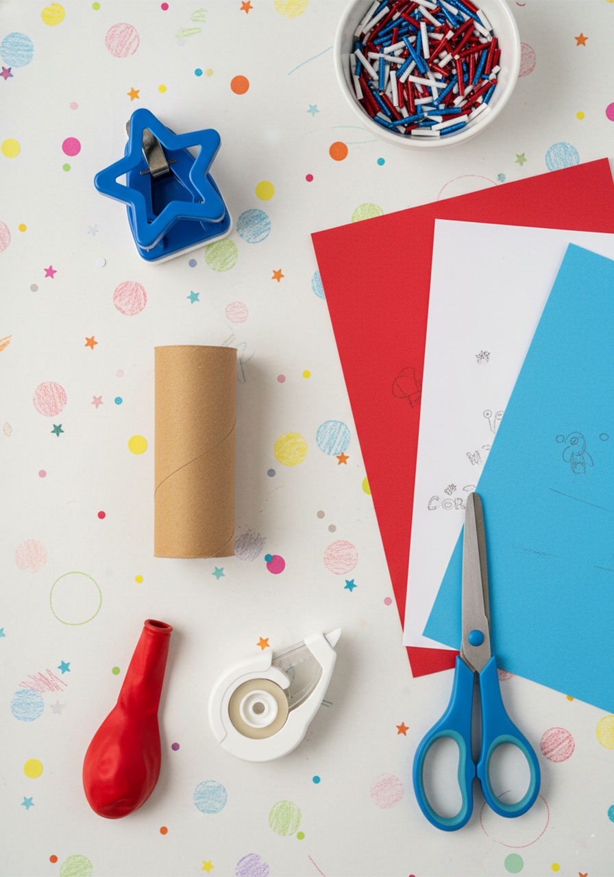 All supplies needed for DIY 4th of July confetti poppers including toilet paper roll balloon colored paper star punch and confetti