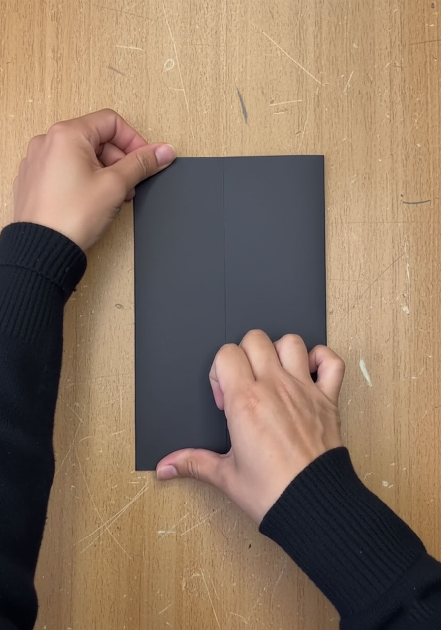 Hands folding black cardstock into a gatefold shape for DIY tuxedo Father's Day card step 1