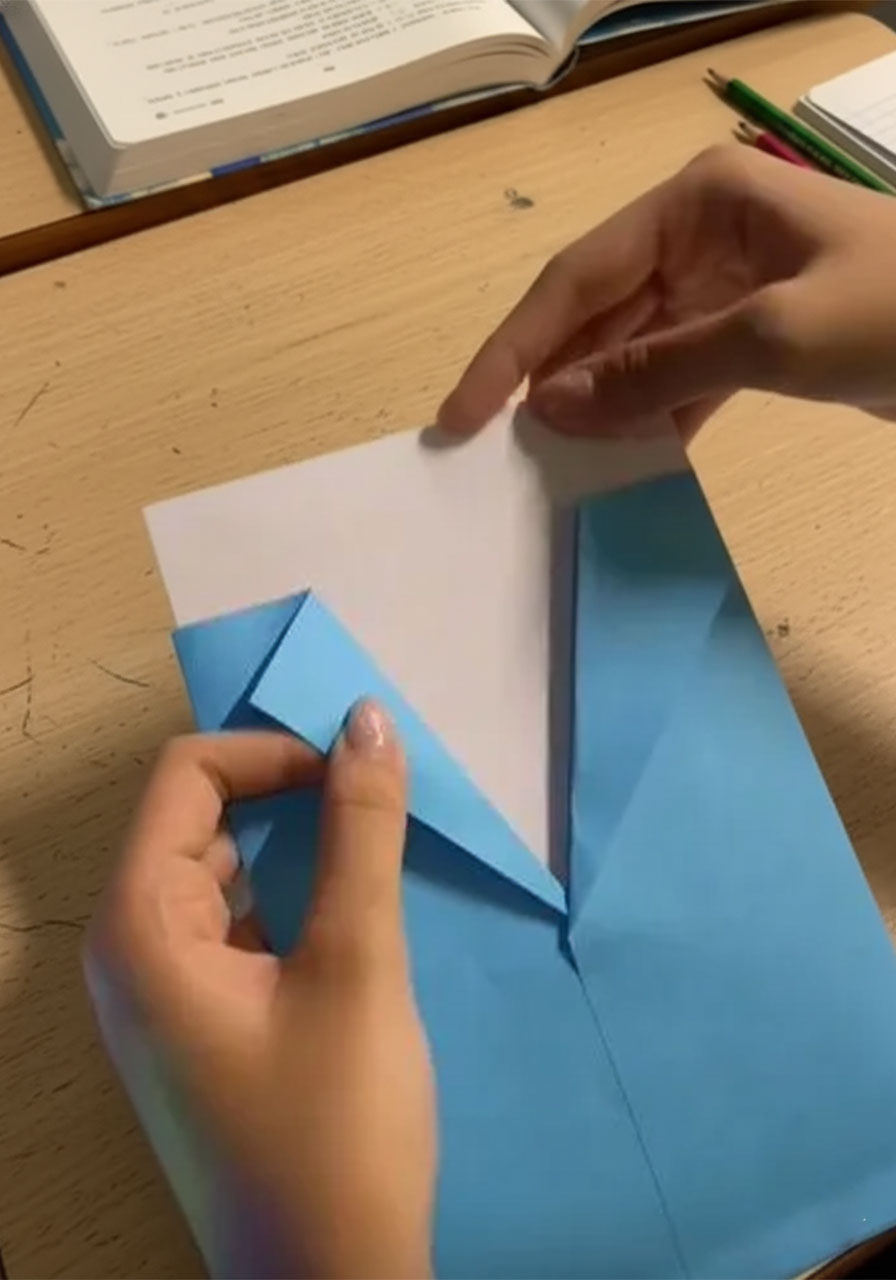 Hands folding white paper into a V-shaped shirt collar for a DIY Father's Day card insert, showing the diagonal crease mid-fold step2b