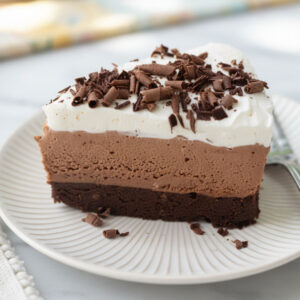 Close-up slice of gluten-free chocolate mousse cake showing three distinct layers: brownie base, chocolate mousse, and whipped cream