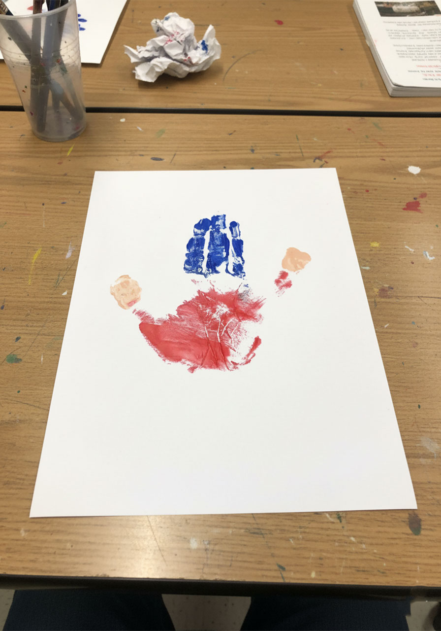 Child pressing painted hand firmly onto white cardstock to create the body stamp for the handprint Mini-Me Dad Father's Day keepsake, Step 2