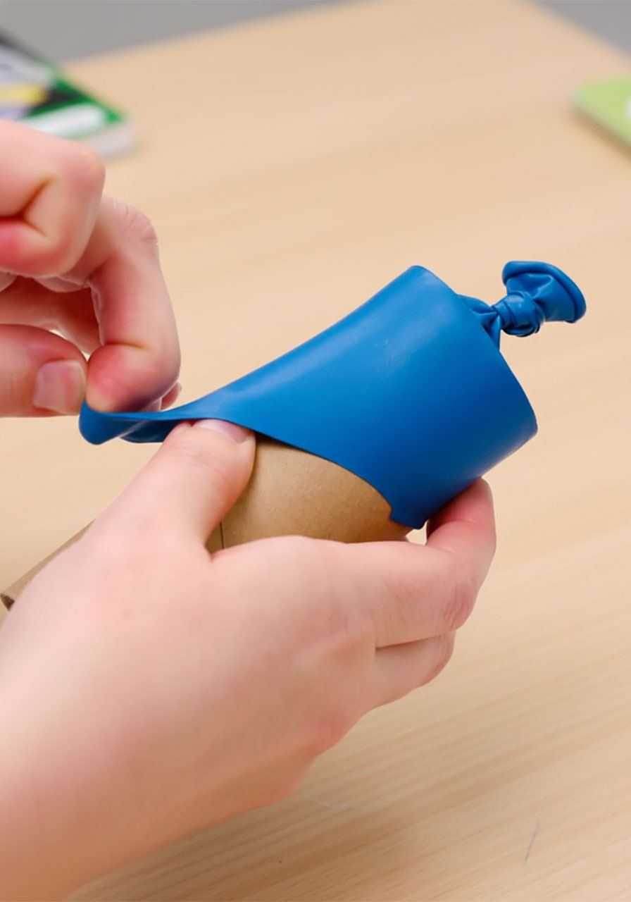 Three-step process showing how to tie cut and stretch a red balloon over a toilet paper roll to make a DIY confetti popper step 1&2c