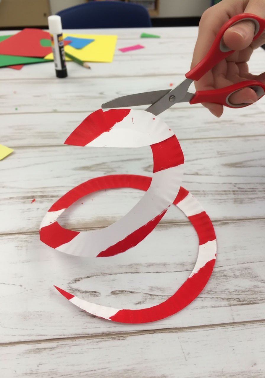 Cutting a red and white striped paper plate into a spiral for a patriotic wind catcher craft step by step