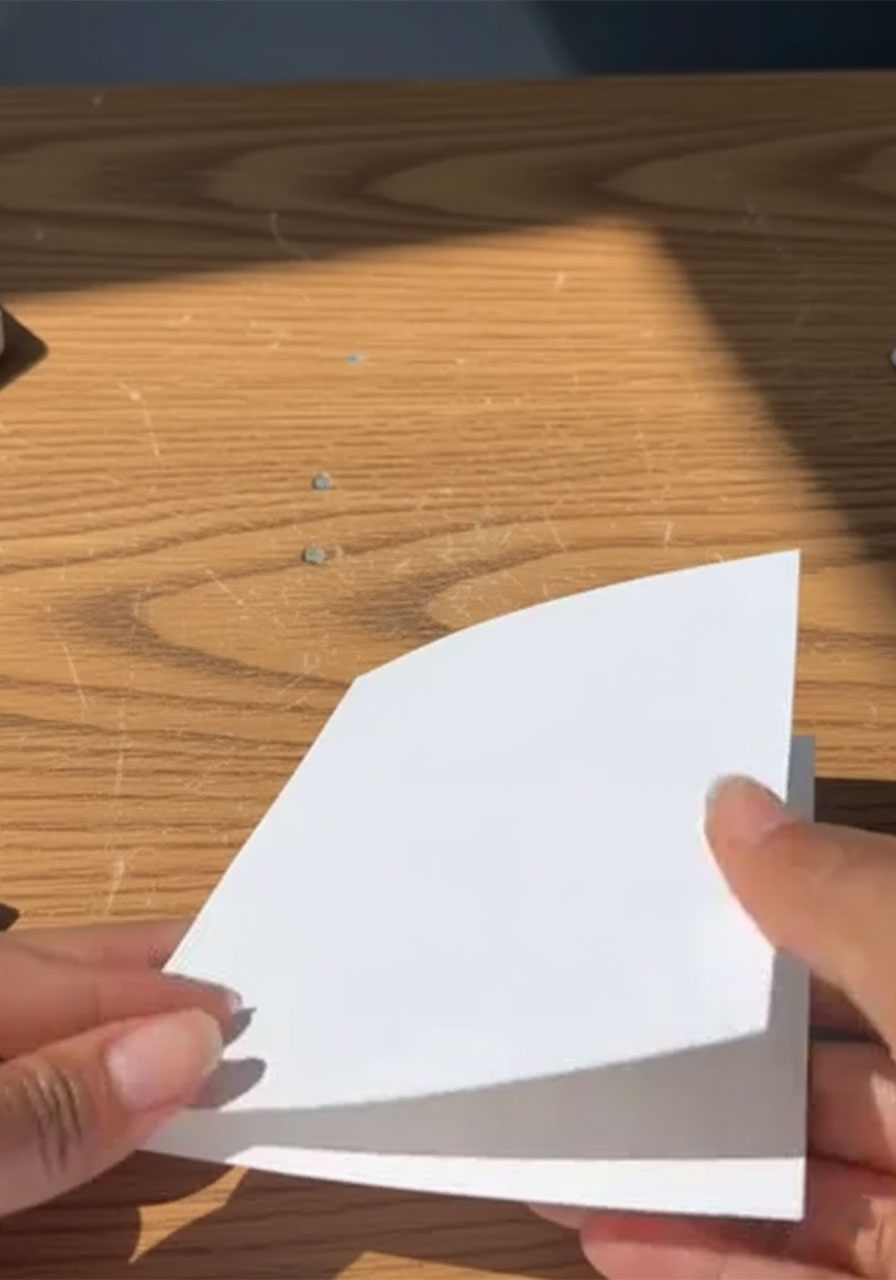 Hands cutting three sets of parallel slits along the folded edge of white cardstock to create the 3D pop-up card mechanism step1a