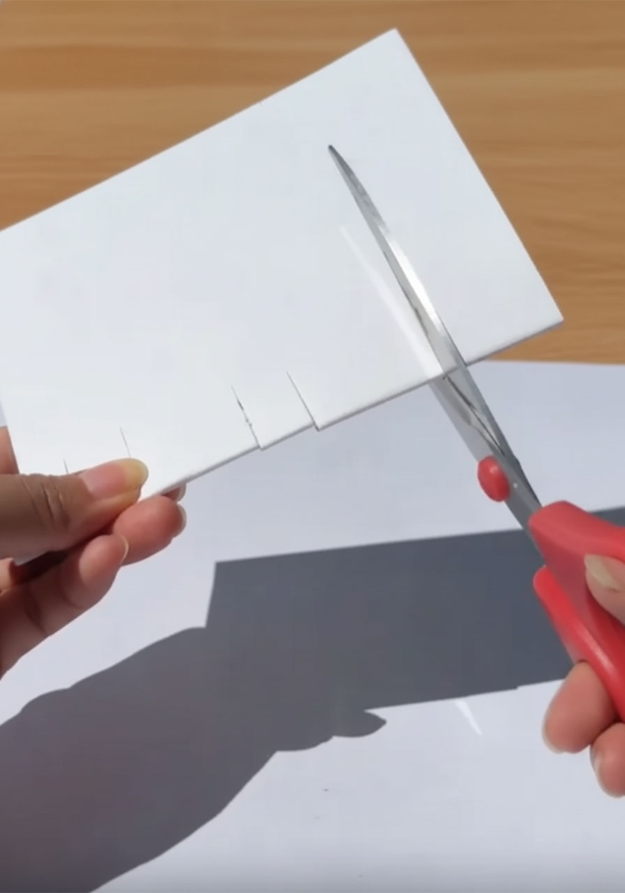 Hands cutting three sets of parallel slits along the folded edge of white cardstock to create the 3D pop-up card mechanism step1b