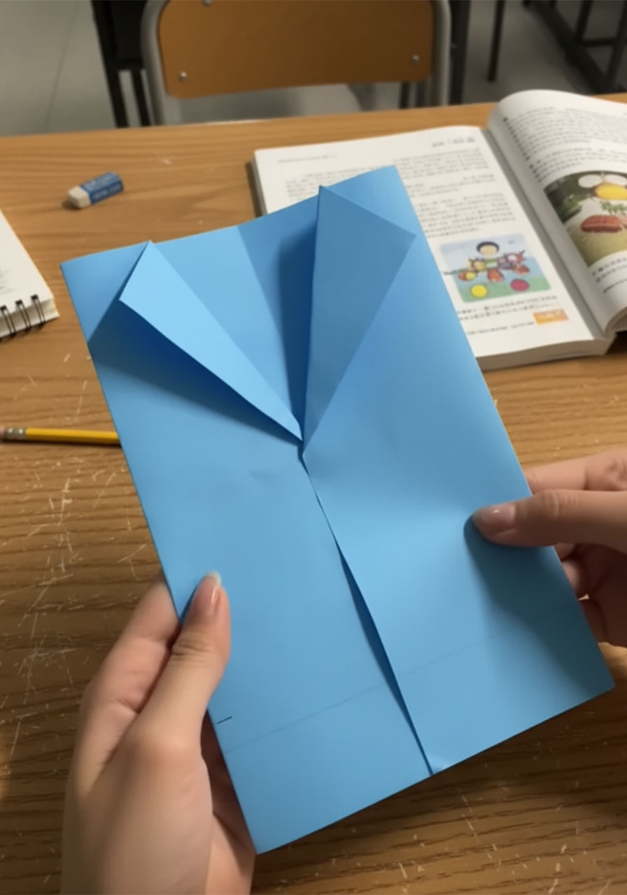 Hands folding royal blue paper inward to form the suit jacket base for a DIY Father's Day card, with a ruler for reference on a white table step1b