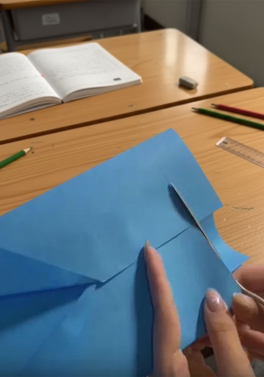 Hands folding royal blue paper inward to form the suit jacket base for a DIY Father's Day card, with a ruler for reference on a white table step1e