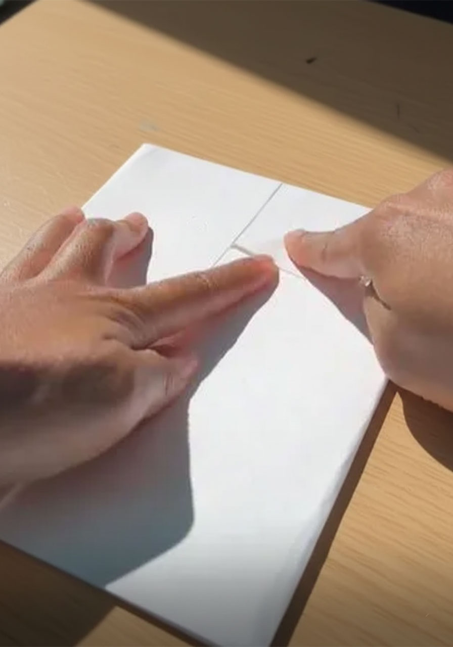 Hands folding white cardstock into dress shirt collar shape for DIY Father's Day card craft tutorial step1b