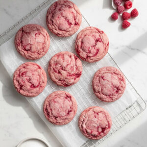 Gorgeous pink raspberry sugar cookies on a cooling rack surrounded by frozen raspberries — easy gluten free dessert recipe