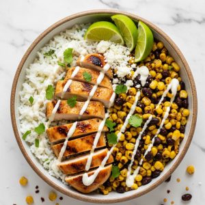 Street corn chicken rice bowl with grilled chicken, charred corn, black beans, cotija cheese and lime crema, overhead view