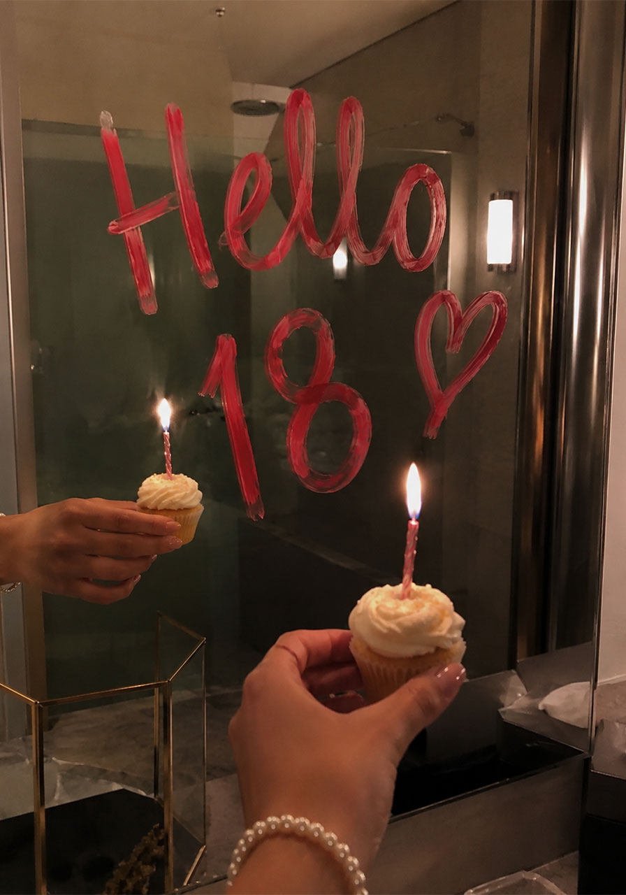 Hello 18 written in lipstick on mirror with birthday cupcakes with lit candles