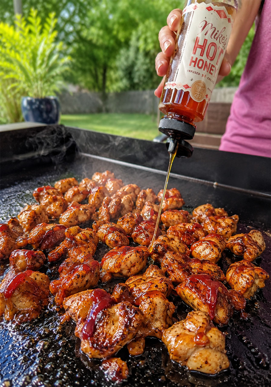 Drizzling Mike's hot honey onto cooked BBQ chicken bites on a Blackstone griddle to make quesadilla filling