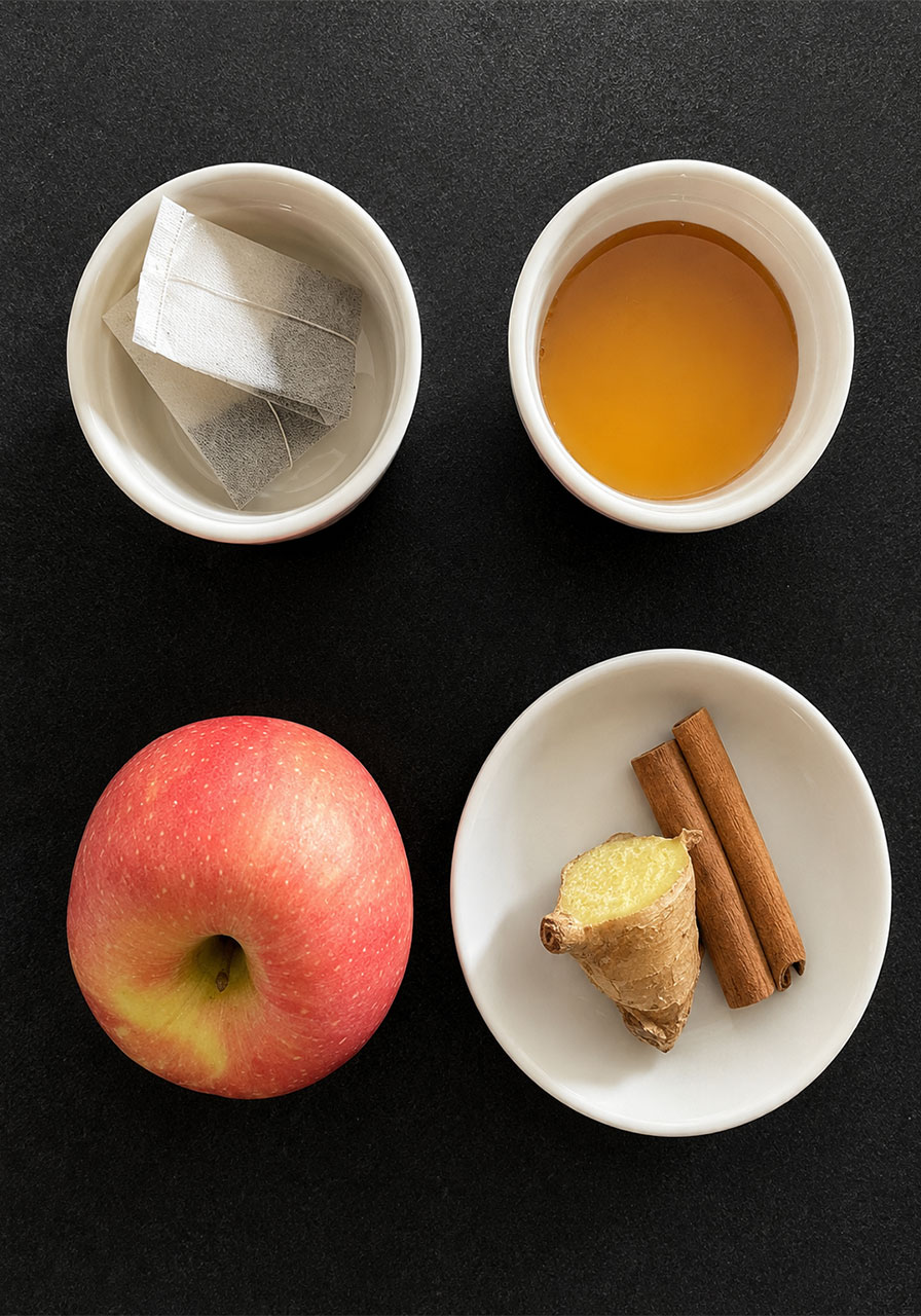 Ingredients for apple cinnamon iced tea including black tea bags, honey, fresh apple, ginger, and cinnamon sticks