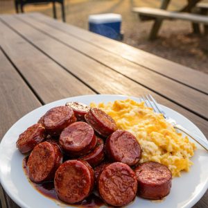 Baked BBQ sausage glazed with sticky caramelized sauce served on a white plate with hashbrown casserole