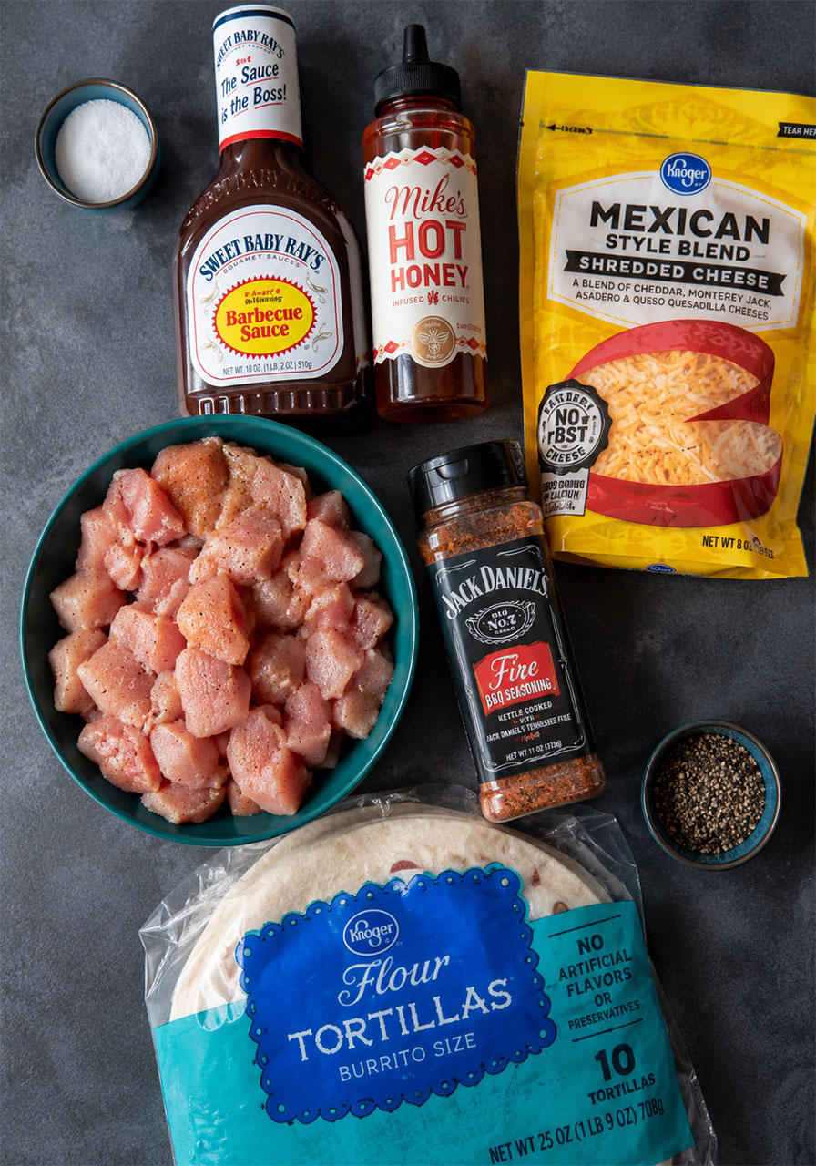 All ingredients for Blackstone hot honey BBQ chicken quesadillas including chicken thighs, BBQ sauce, hot honey, shredded cheese, and flour tortillas
