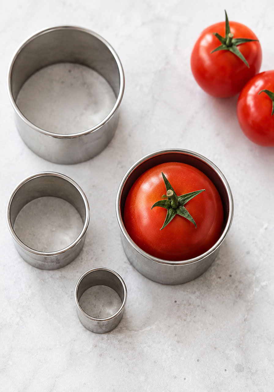 Cocktail tomato fitting snugly inside a round cookie cutter to determine the correct size for BLT tea sandwiches