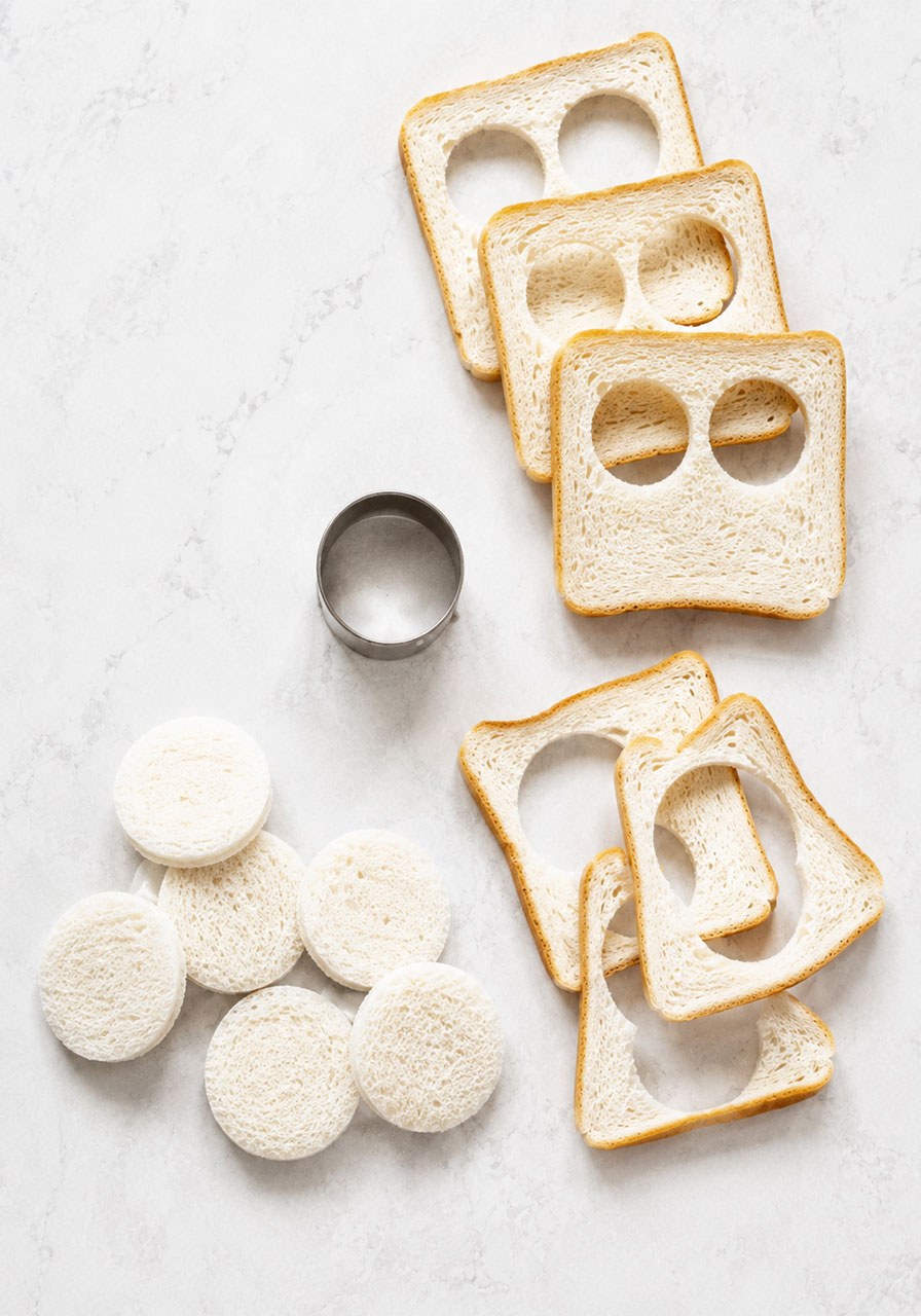 Round crustless white bread circles cut with a cookie cutter next to the leftover bread slices, ready for BLT tea sandwich assembly
