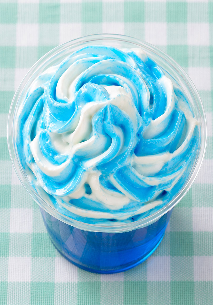 Clear party cup with blue Jello topped with freshly swirled blue-and-white whipped cream waves – step four of the Swimming Bears pool party dessert recipe