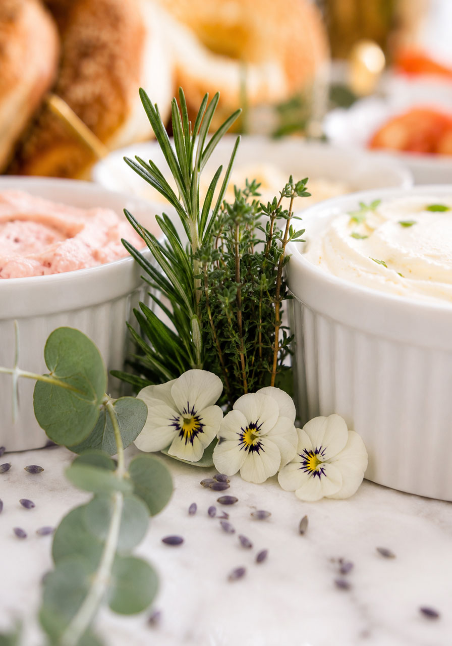 Fresh rosemary, thyme, and edible flowers used to style a bridal shower bagel bar display