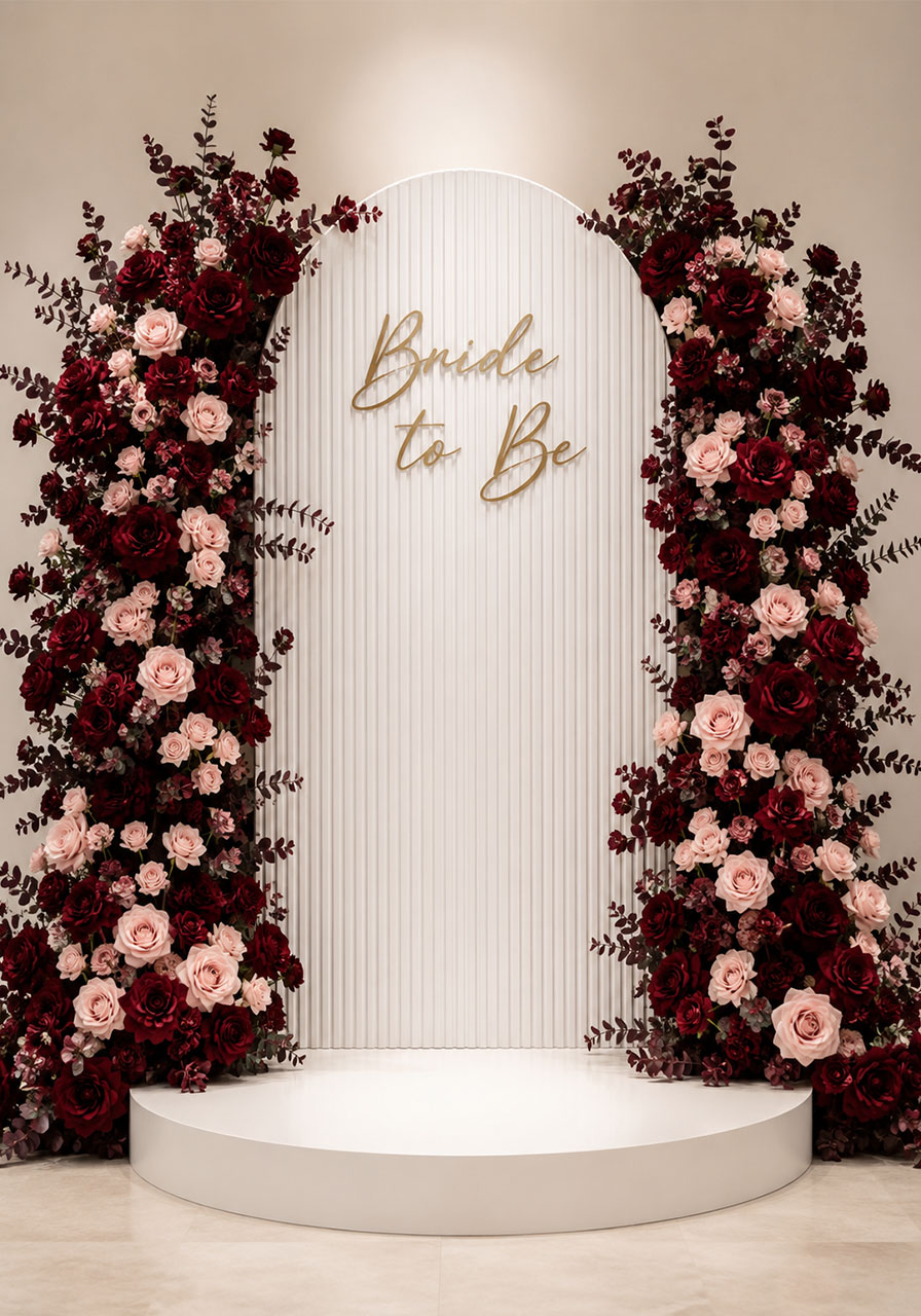 White arch backdrop with deep red and blush rose floral clusters and gold Bride to Be lettering for bridal shower photos