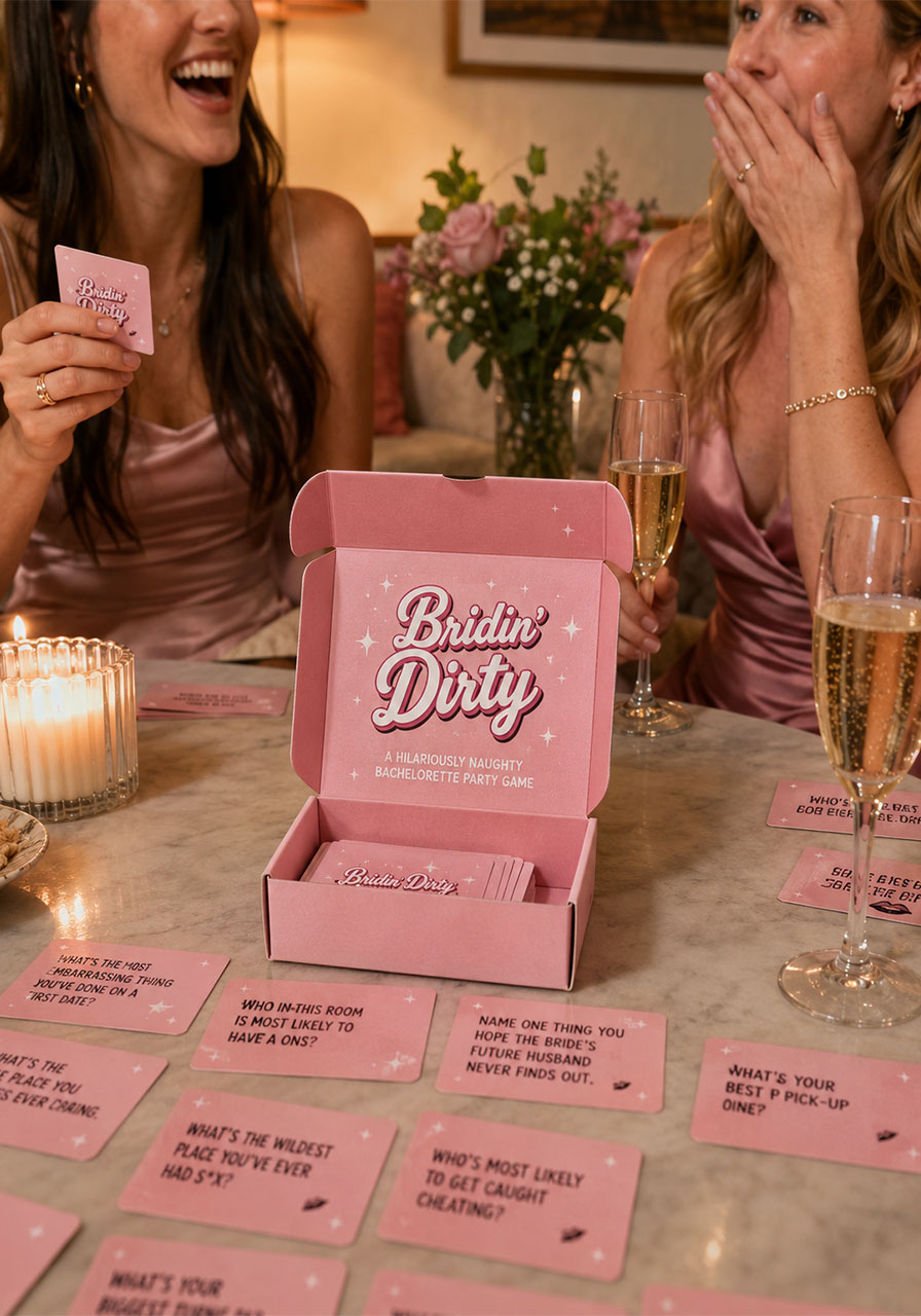 Women laughing playing Bridin' Dirty bachelorette card game with pink game cards spread on coffee table