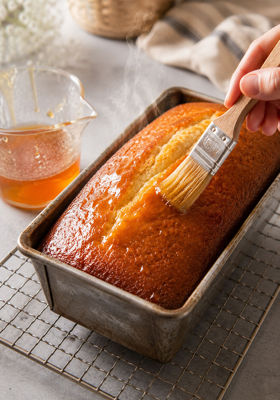 Brushing warm honey syrup over freshly baked tea cake loaf for extra moisture