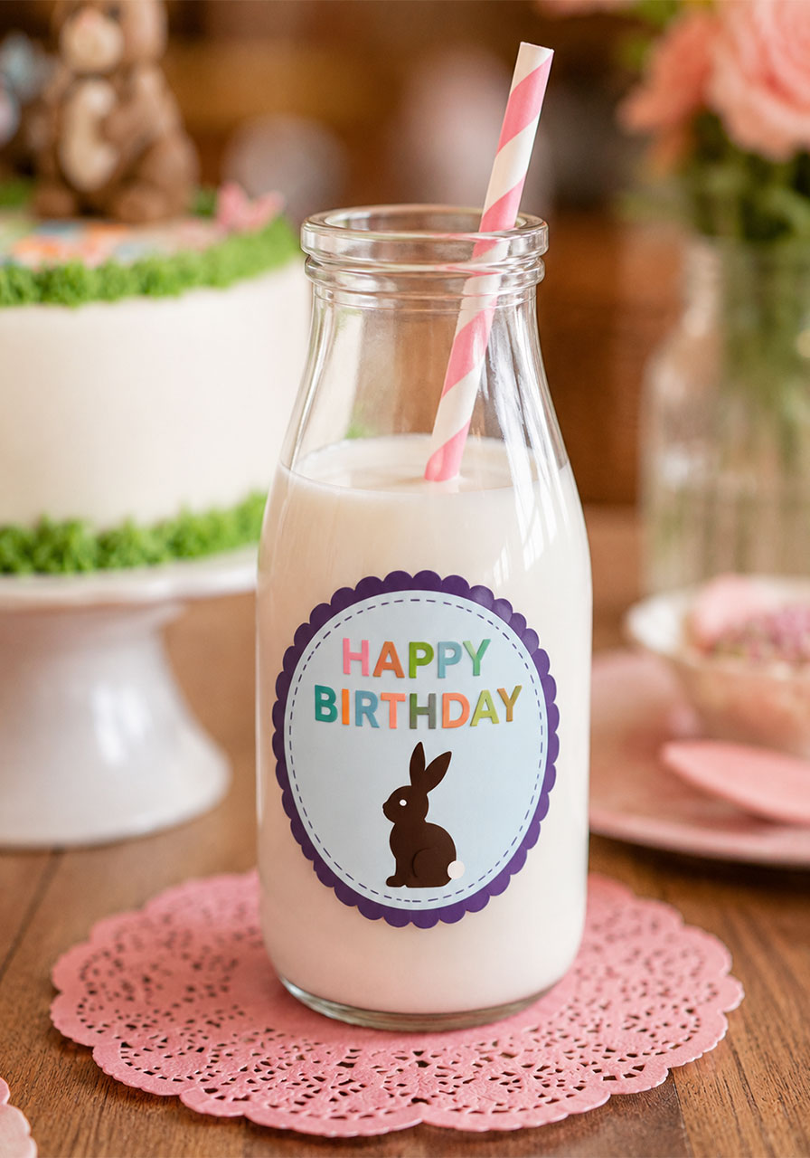 Personalized Happy Birthday glass milk bottle with bunny label and pink striped paper straw for a bunny and butterfly birthday party table