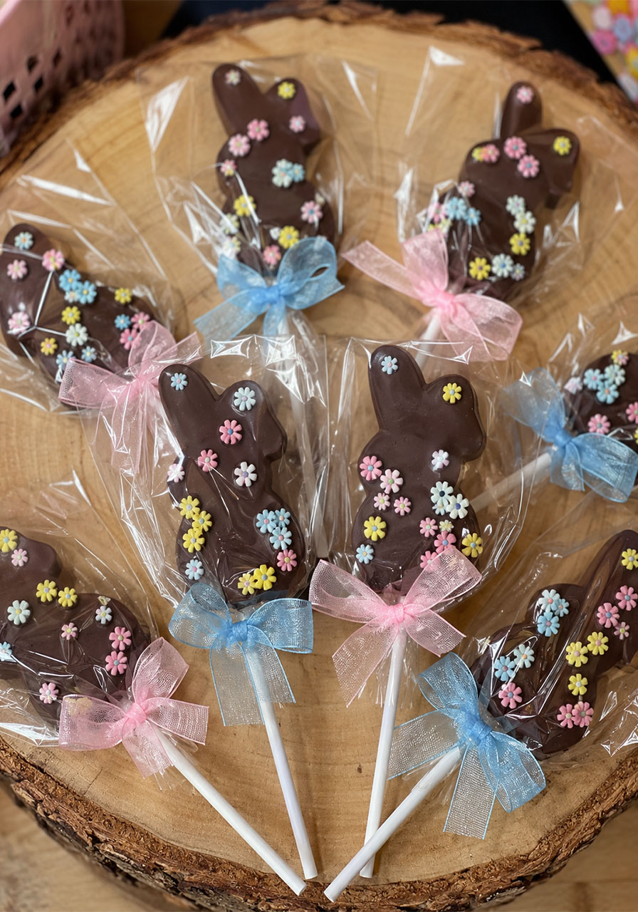 Chocolate bunny pops decorated with pastel sugar flowers and wrapped with pink and blue ribbon bows as party favors for a bunny birthday party