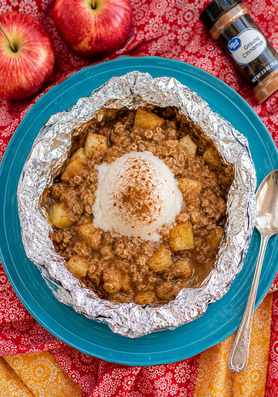 Overhead view of an opened campfire apple pie foil packet topped with vanilla ice cream on a teal plate