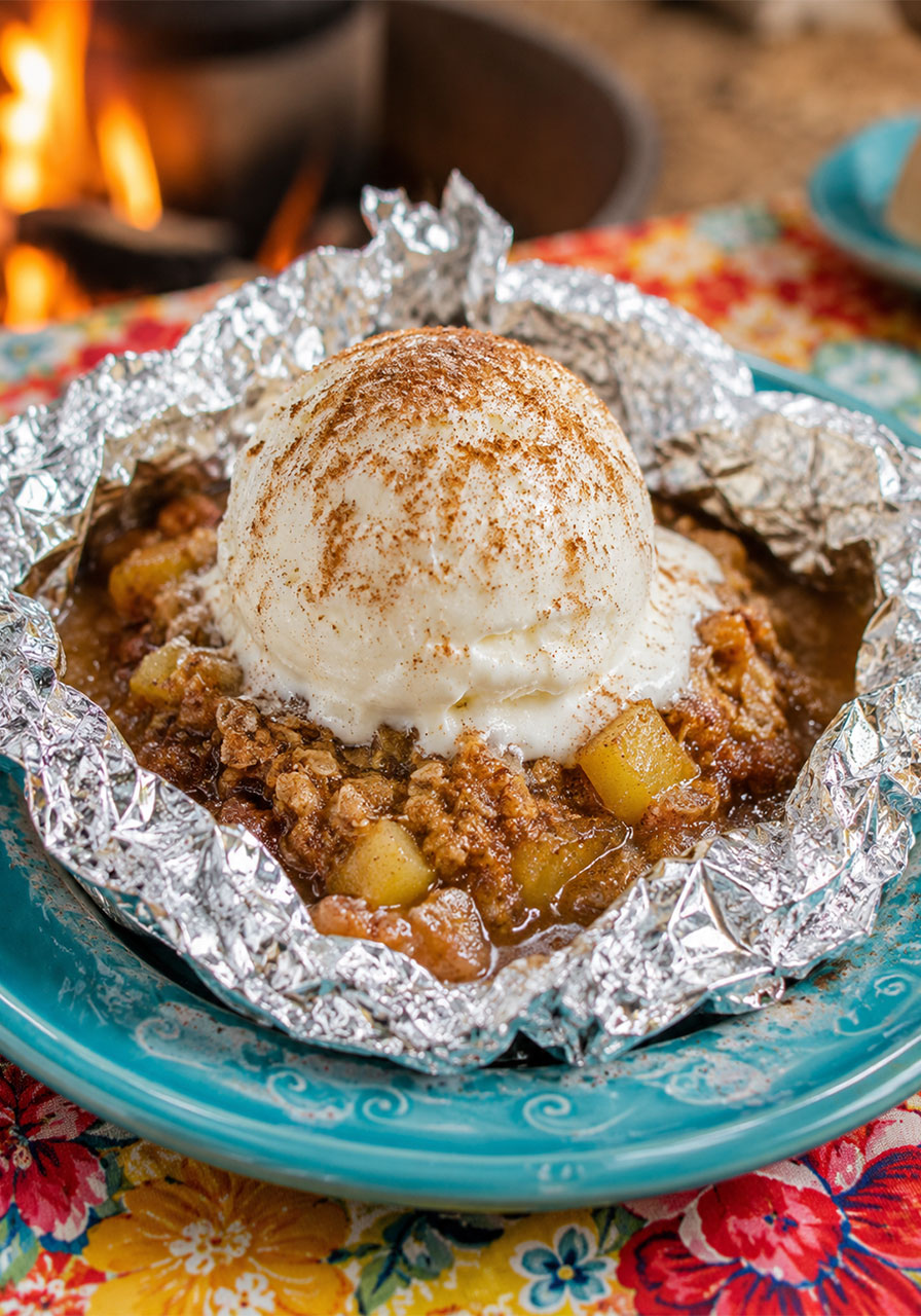 Campfire apple pie foil packet opened on a teal plate topped with a melting scoop of vanilla ice cream