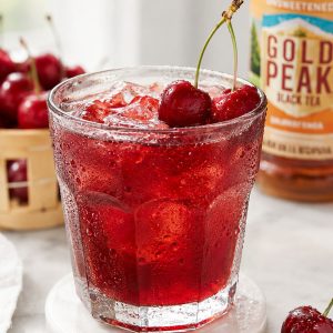 Close-up of a cold glass of cherry iced tea with ice cubes, condensation, and fresh cherry garnish