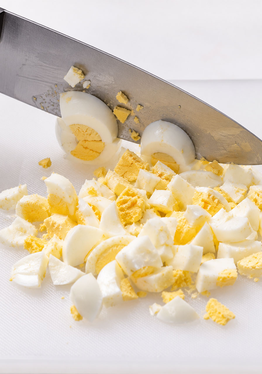 Chopping hard boiled eggs on a white cutting board to the correct rough texture for egg salad tea sandwiches