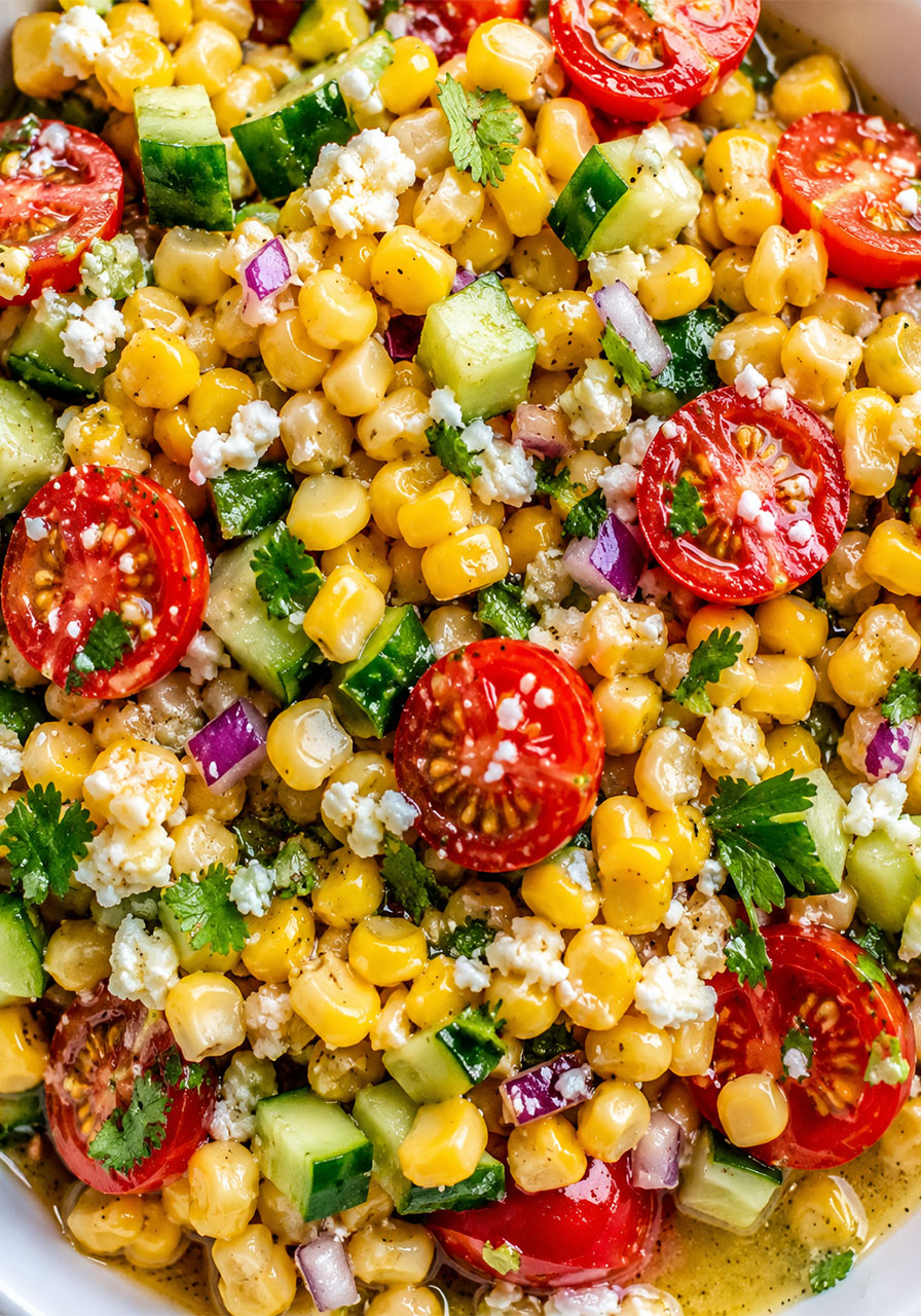 Close-up of fresh corn salad showing corn kernels, cherry tomatoes, and crumbled cotija cheese with lime dressing