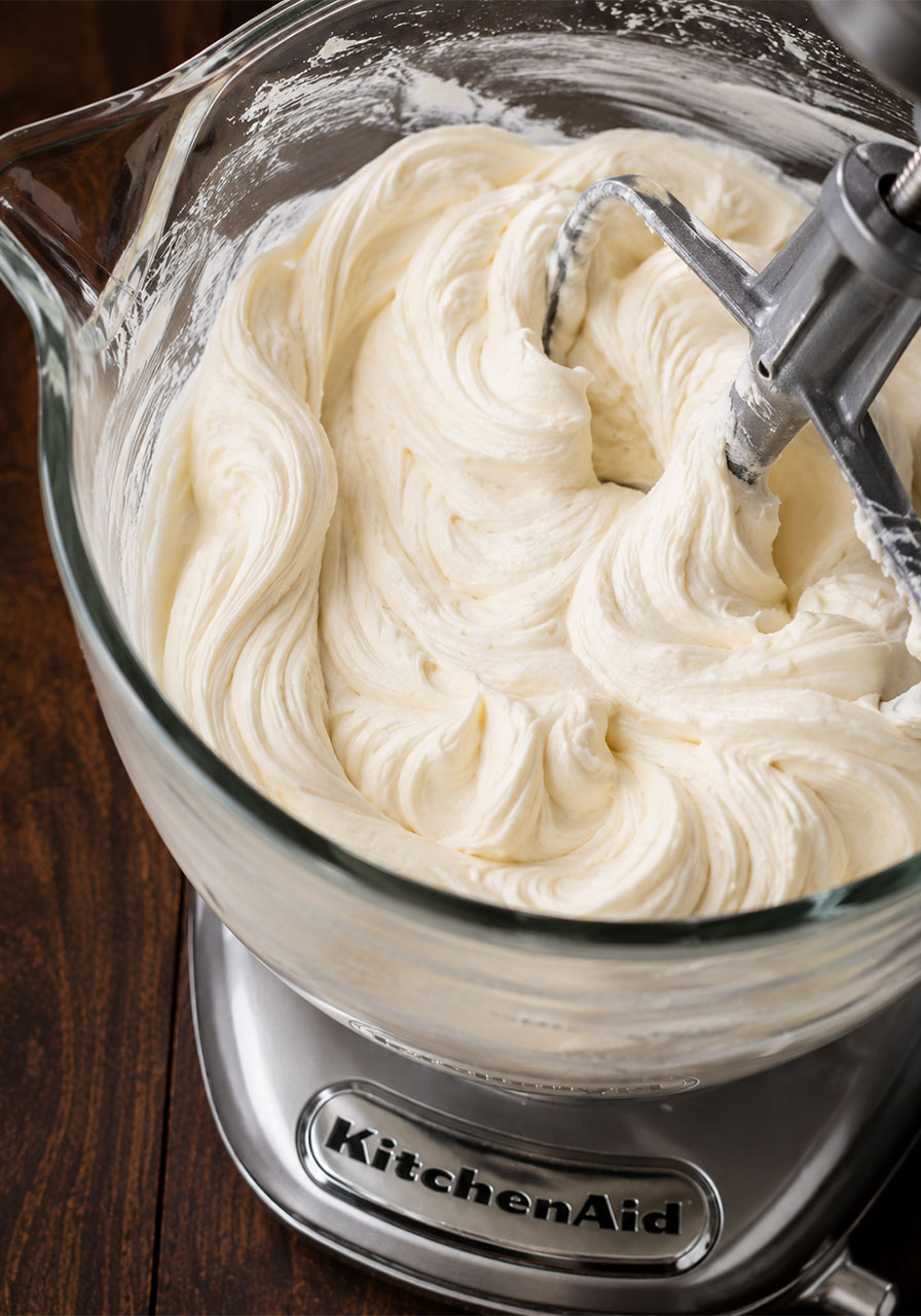 Thick smooth cream cheese frosting with glossy peaks in a KitchenAid stand mixer bowl for brown sugar chai cake
