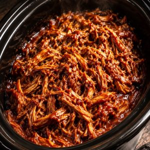 Flavor-loaded crock pot BBQ pulled pork glistening with smoky sauce in a black slow cooker, freshly shredded and ready to serve
