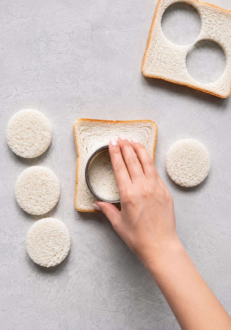 Using a round metal cookie cutter to cut crustless white bread circles for egg salad tea sandwiches