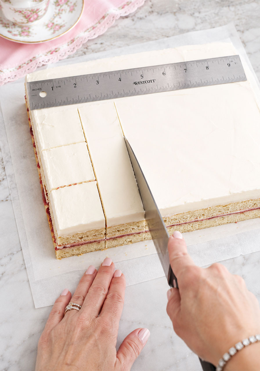 Cutting frozen assembled petit fours cake into uniform 1.25-inch squares with a sharp knife