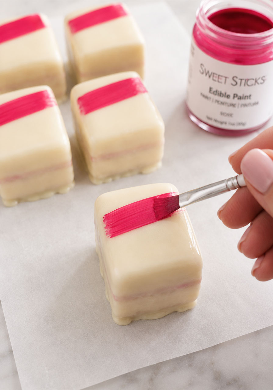 Decorating petit fours with hot pink edible paint brushstroke for elegant party presentation