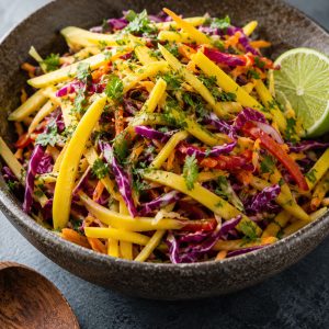 Delicious mango slaw in a rustic ceramic bowl topped with fresh cilantro and a lime wedge, served as a vibrant vegetarian side dish
