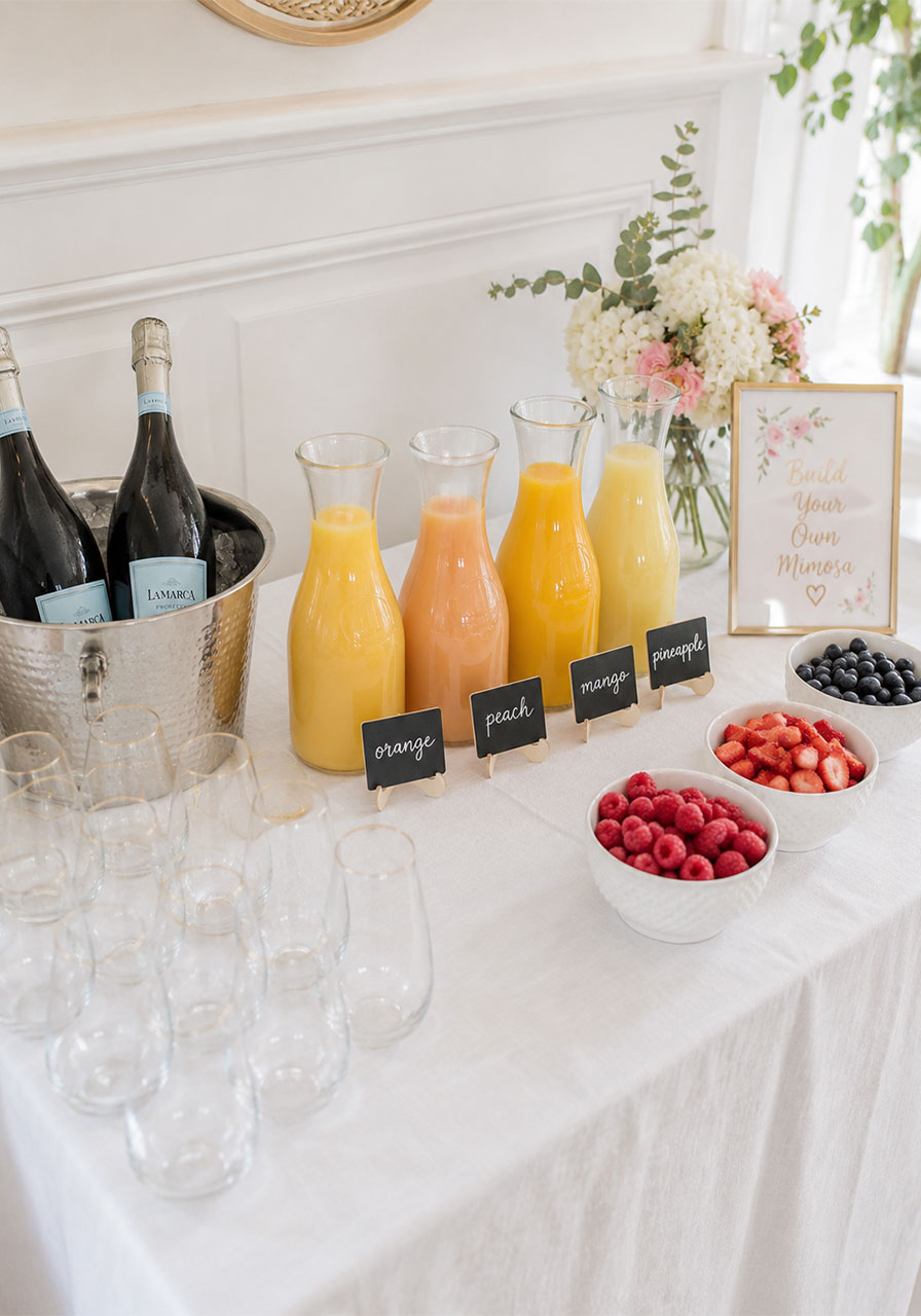 Elegant DIY mimosa bar setup with juice carafes and fresh fruit for bridal shower brunch