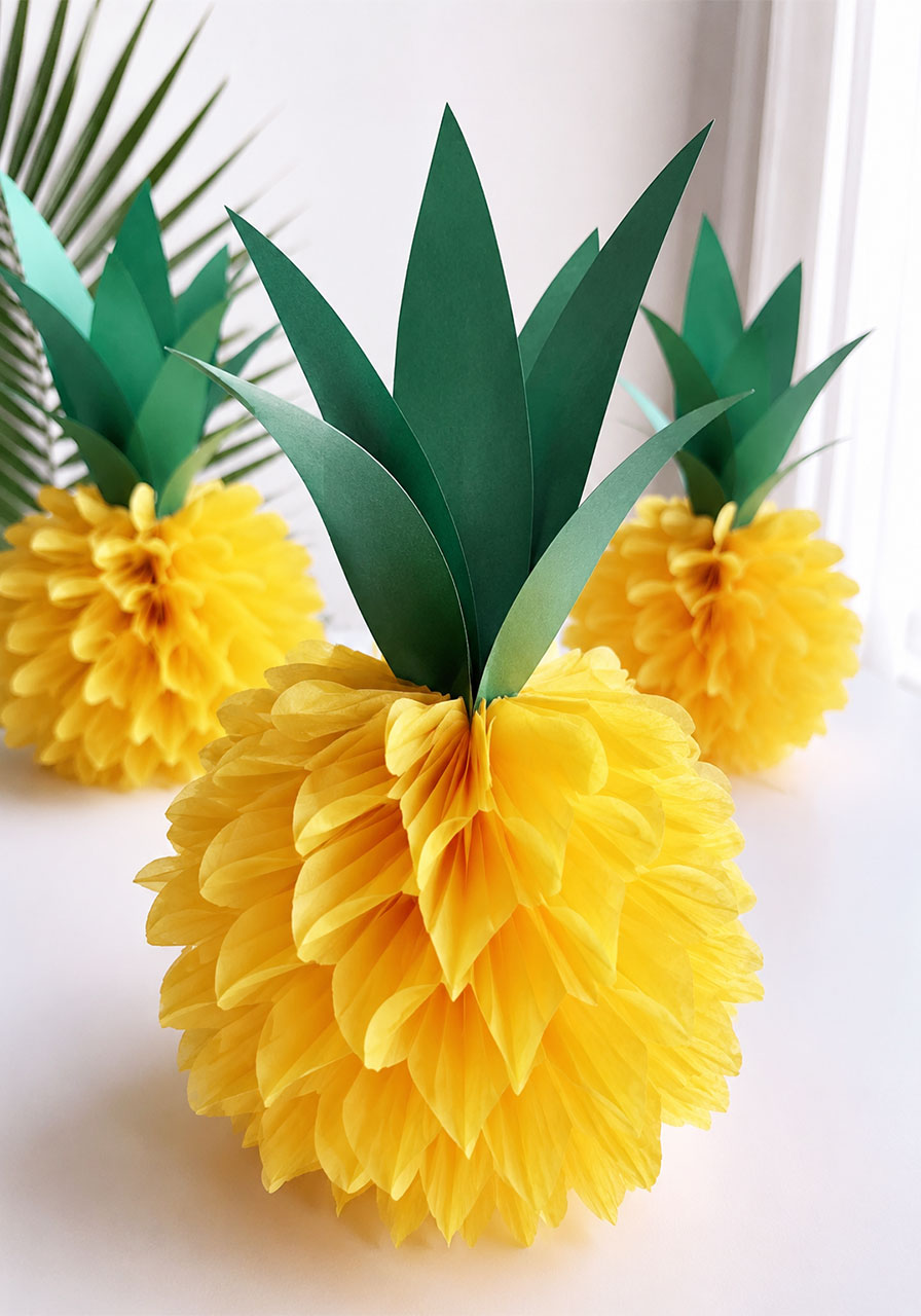 DIY yellow tissue paper pineapple pom-poms with green cardstock leaves for tropical pool party decorations