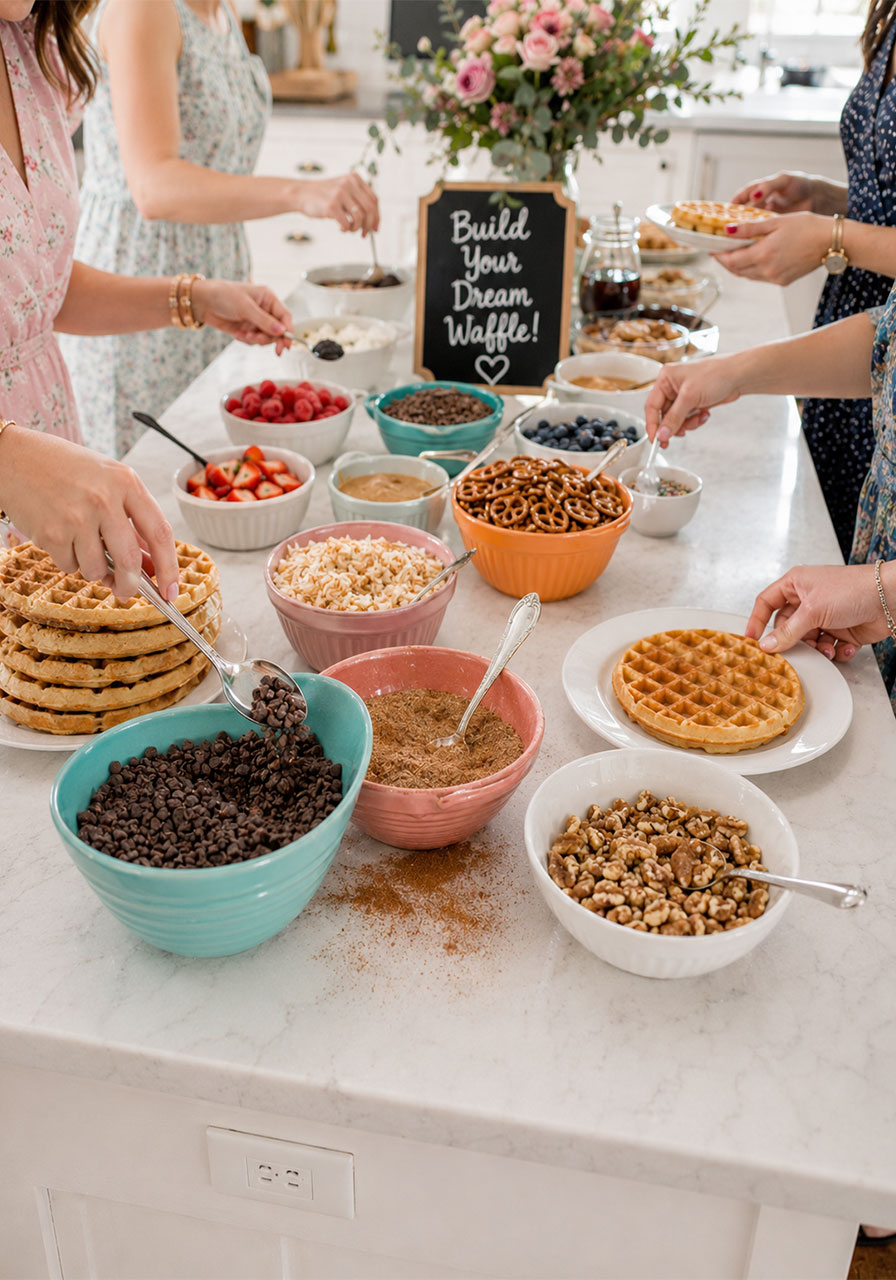 Guests building their own waffles at a DIY topping station at a fun brunch party waffle bar