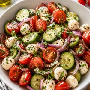 Easy cucumber caprese salad in a white serving bowl with cherry tomatoes, mozzarella, cucumber, and fresh basil