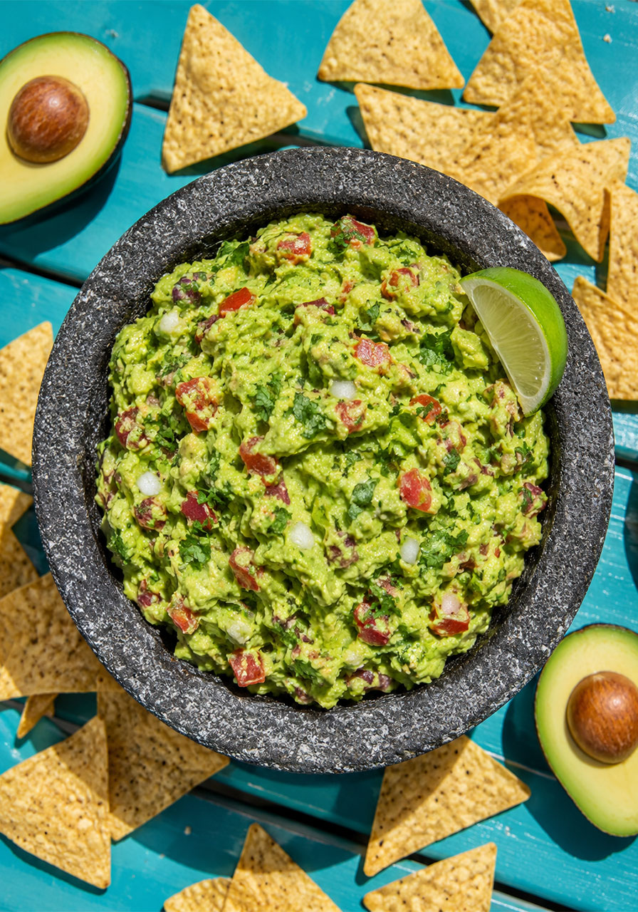 Homemade chunky guacamole in a stone bowl surrounded by tortilla chips for a pool party